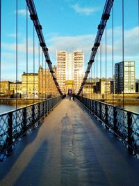 Suspension bridge in city against sky