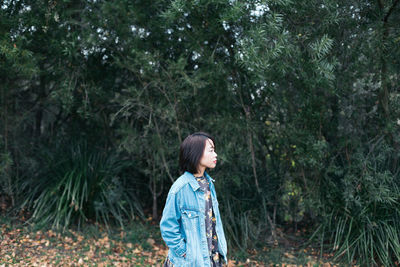 Woman looking away while standing against trees