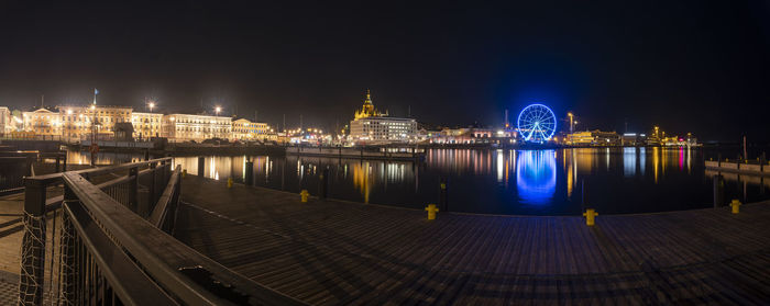 Illuminated city by river against sky at night