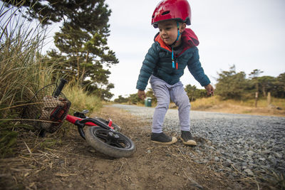 Toddler boy leans over to pick up bike.