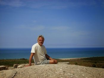 Portrait of man sitting on rock against sea and sky