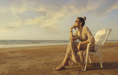 Woman sitting on beach by sea against sky