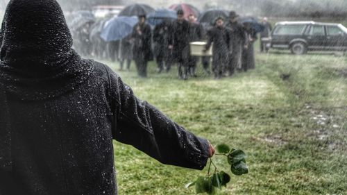 Rear view of man holding leaves with people carrying coffin at cemetery during snowfall