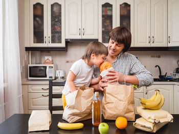 Family sorts out purchases in the kitchen. father and son tastes products in bags craft paper. 