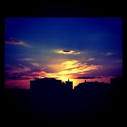 Silhouette of buildings against cloudy sky at sunset