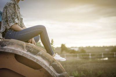 Low section of woman sitting on land against sky