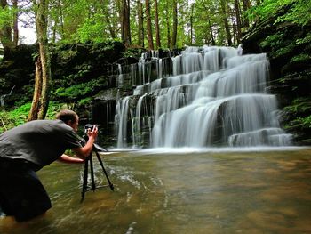 Man photographing waterfall through camera in forest