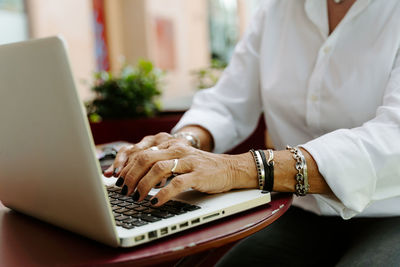 Cropped unrecognizable female freelancer sitting at table in outdoors cafe and working remotely on project while using netbook