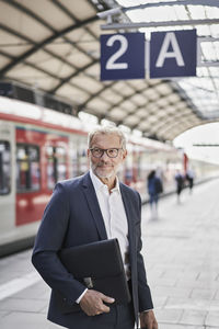 Male professional looking away while holding laptop at railroad station