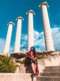 Woman sitting by built structure against sky