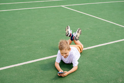 The boy is lying on the floor and playing with the phone