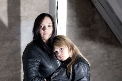 Portrait of daughter embracing mother while standing against wall