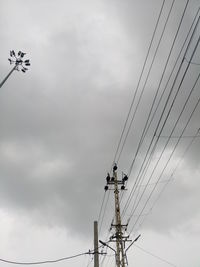 Low angle view of electricity pylon against cloudy sky