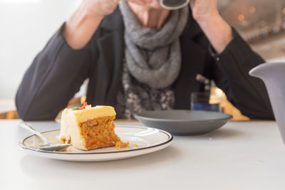 Midsection of woman sitting by cake in plate on table at restaurant