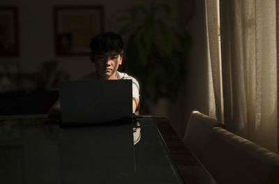 Portrait of teenage asian boy using laptop indoor with sunlight and shadow