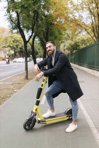 Smiling young man leaning on electric push scooter at bicycle lane