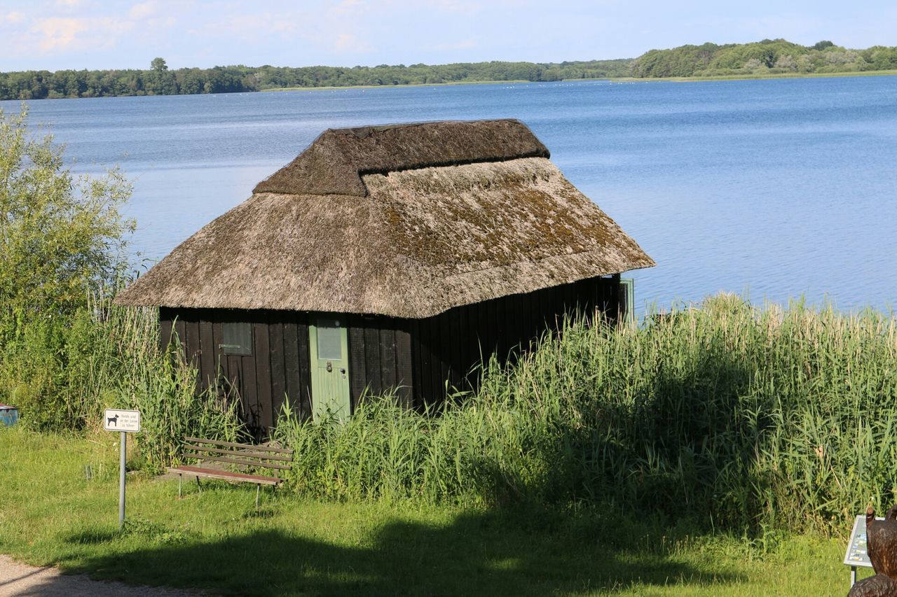 grass, water, tranquil scene, tranquility, built structure, nature, field, scenics, beauty in nature, architecture, plant, wood - material, green color, day, building exterior, sky, lake, growth, landscape, outdoors