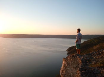 Man standing on mountain by sea against clear sky during sunset