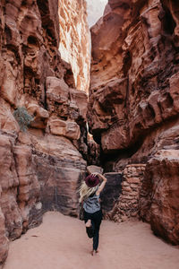 Rear view of young woman standing by rock formation