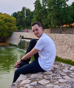 Portrait of young man sitting on retaining wall