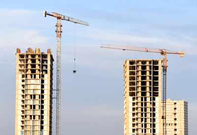 Low angle view of crane by building against sky