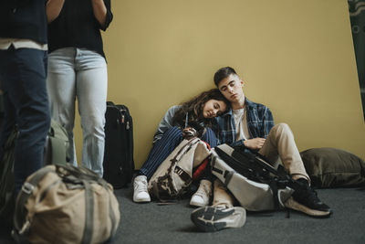 Brother and sister taking rest while sitting amidst luggage near yellow wall