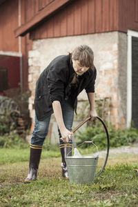 Full length of woman filling water with hose at farm