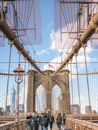 People on suspension bridge against cloudy sky