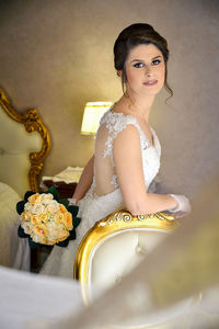 Portrait of bride standing holding bouquet while standing by chair