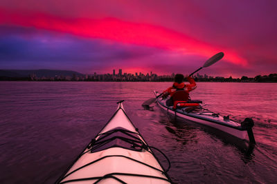 Man on boat in sea against sky during sunset