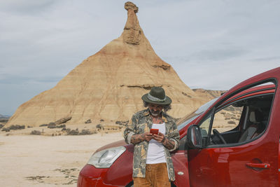 Middle aged traveler looking at cell phone in desert landscape of bardenas reales.