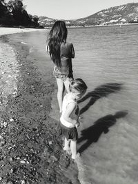 Rear view of young woman with girl standing at lakeshore