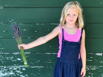 Portrait of cute girl standing with plants against wooden wall