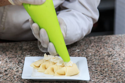 Cropped image of person icing food in plate on table