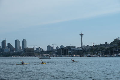 People on river by buildings against sky