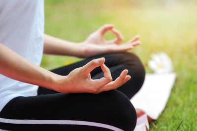 Midsection of woman meditating in lotus position on grassy field