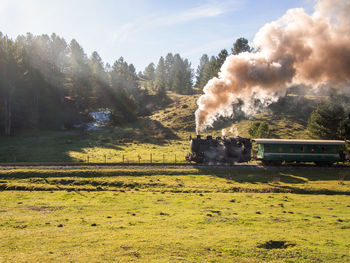 Smoke emitting from train on field against sky