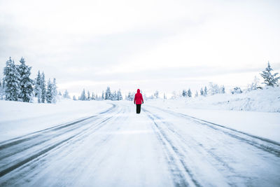 Rear view of person walking on snow covered street against sky