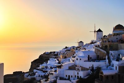 Traditional windmills amidst houses at santorini against sky during sunset