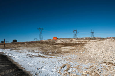 Electricity pylon on land against clear blue sky