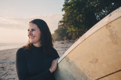 Smiling mature woman carrying surfboard at beach