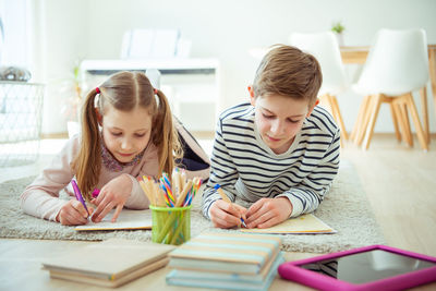 Cute siblings studying while lying down on floor