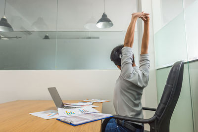 Rear view of woman using digital tablet while sitting on table