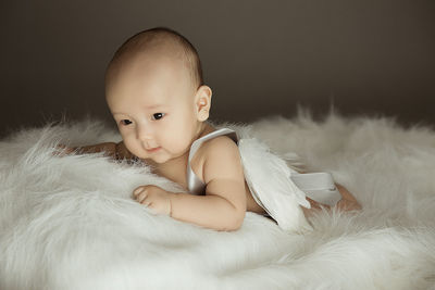 Cute baby boy wearing artificial wing while lying on fur blanket at home