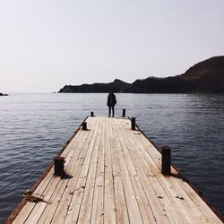 Woman standing on wooden jetty on tranquil sea