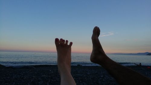 Low section of person on beach against sky during sunset