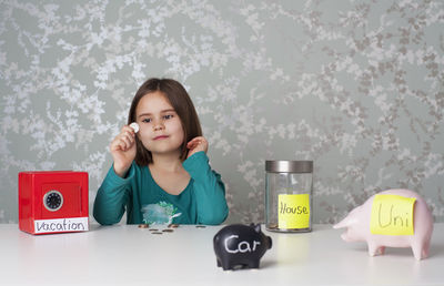 Portrait of girl sitting on table against wall