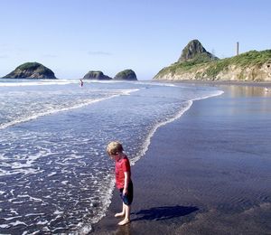 Side view of boy standing on shore at beach against sky