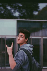 Portrait of young man making horn sign outdoors