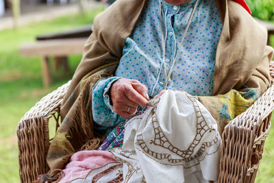  middle section of woman embroidering sitting in basket